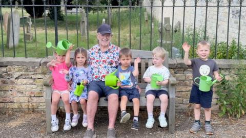 Man is a flower patterned shirt sitting with children on a bench