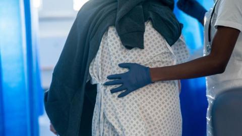 Image shows a patient being led by a member of staff on a NHS hospital ward at Ealing Hospital in London