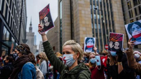 A woman wears a protective face mask and holds a banner as she participates in a National strike for the seventh day of protests against the Constitutional Court ruling