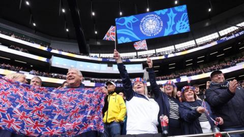 Fans wave Union Jack flags following the national anthem for the Coronation of Charles III prior to the match between Tottenham Hotspur and Crystal Palace at Tottenham Hotspur Stadium