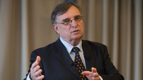 David Moffett wears a dark suit with blue and red tie