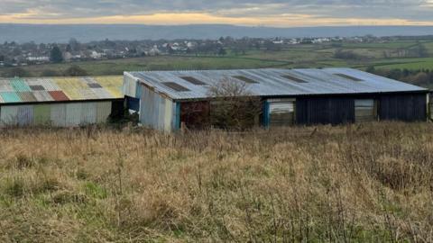 A scrubby field with some out buildings