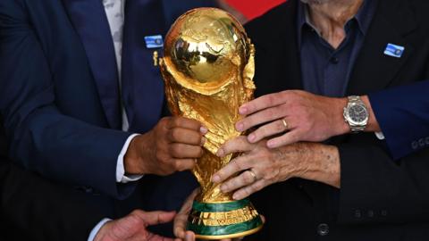 Four hands hold the gold World Cup trophy.