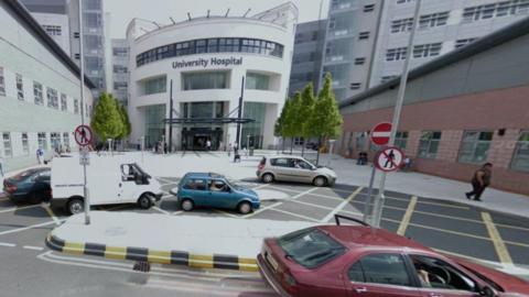 University Hospital, with red, blue, white and silver vehicles in the foreground near a no-entry sign. The University Hospital name is on a building near the back of the photo.