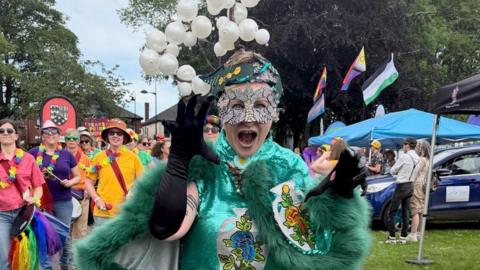A participant is dressed in a bright green outfit with fur trim and is wearing a mask and black gloves