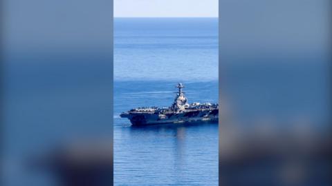 A large grey warship on open water with many military aircraft on board.