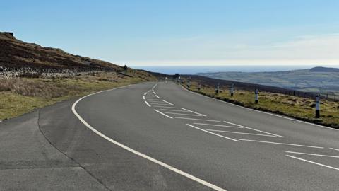 A section of the Mountain Road at Windy Corner looking in the direction of Keppel Gate on a clear day with blue sky above.