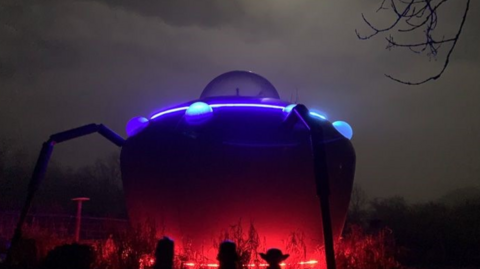 UFO-style accommodation pod lit up at night with red and purple lights shining out
