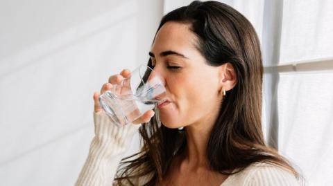 A brown haired woman drinks a glass of water.