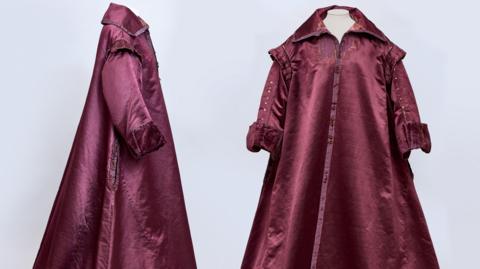 A side and front view of a 1600s era gown. It is a burgundy colour and has a collar.