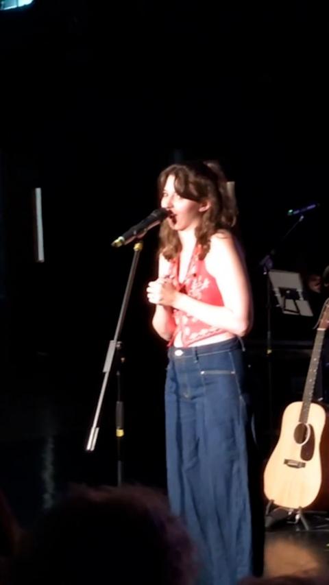 Hannah Richards - woman in red bandana top and jeans, speaking into a microphone on stage