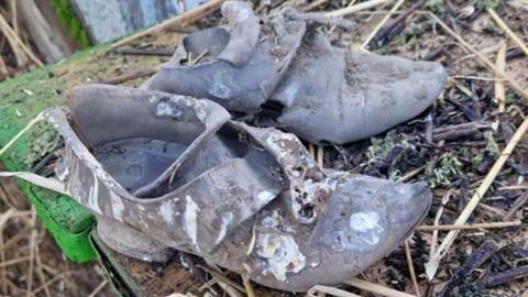 A pair of old shoes placed on a wooden table covered with thatch straws. They are discoloured and worn off. 