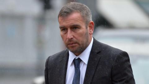 Scott Nugent - a man with short dark hair, wearing a suit, walking towards court