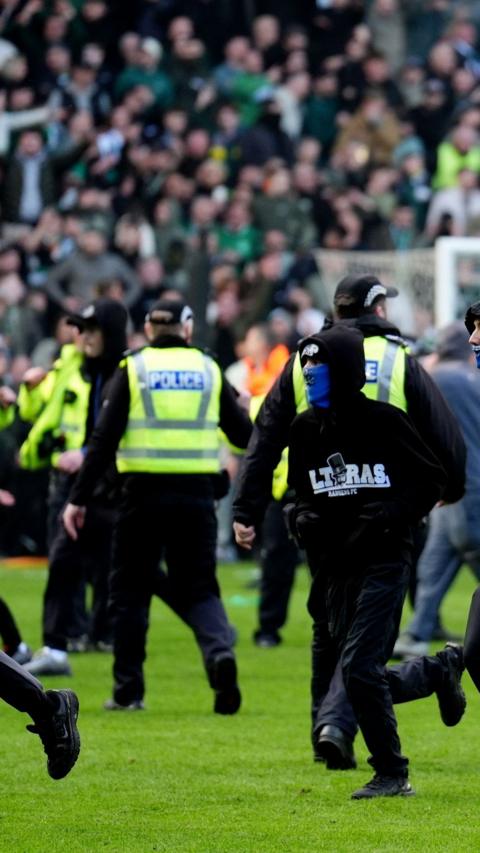 Masked football fans running on football pitch as police attempt to intercept them