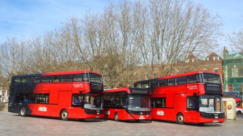 Three red electric buses lined up in front of buildings in Salisbury. 