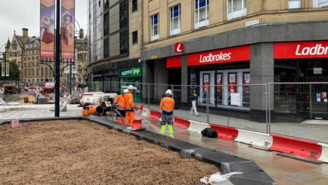 Workmen in orange hi-vis jackets one of the betting shops on Broadway