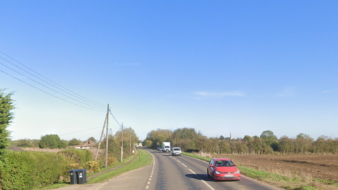 A streetview of the A10, with a blue sky above. The low sun is casting a shadow over the passing cars which are travelling towards the camera.
