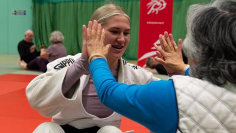 An older person learning judo with other older people in the background out of focus