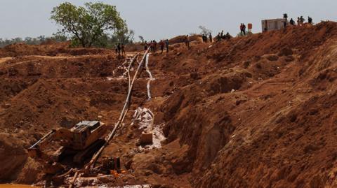 Onlookers peer down at a crane excavating the site of a waterlogged gold mine, which collapsed in a landslide.