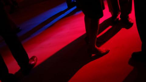 People's legs on a darkly-lit dance floor.