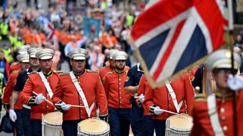 An Orange Order parade, in Glasgow, with flags, and men in orange jackets with drums.