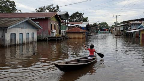 A girl paddles her canoe through a street flooded by the rising Solimoes river