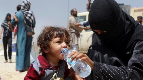 A displaced Iraqi woman helps a child drink water at a camp outside Irbil (15 July 2016)