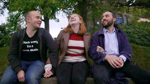 Three people sitting, holding hands