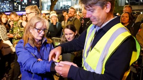 A steward puts a wristband on the wrist of the last woman to be let in the queue