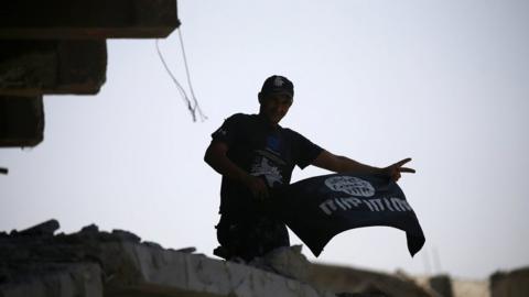 A member of Iraqi security forces celebrates as he holds a flag of Islamic State militants on the top of a destroyed building from clashes in the Old City of Mosul, 10 July
