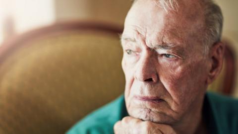 Man in deep thought sat in a chair in a care home