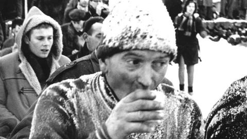 A competitor at the Elfstedentocht sips a drink while covered in snow