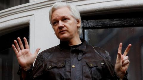 Julian Assange spreads his hands while standing on the balcony of the Ecuadorian embassy