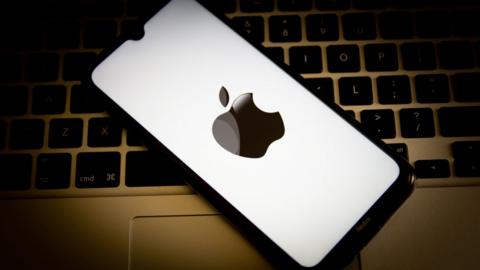 An Apple iPhone displaying the Apple logo is laid on top of a Macbook keyboard