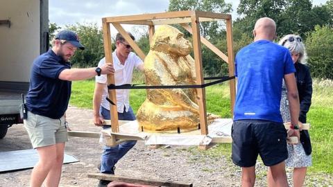 The sculpture being carried by workers