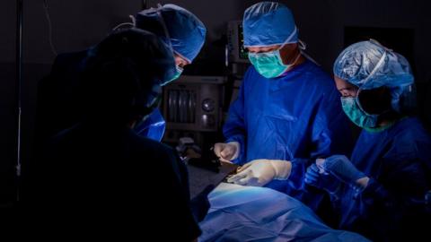 Generic surgical team in blue scrubs performing operation on patient in hospital