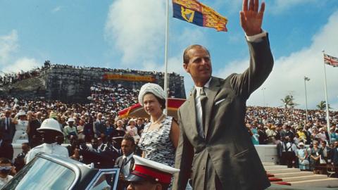 Queen Elizabeth II and her husband Prince Philip wave from an open-top convertible at Clifford Park, Nassau, Bahamas, 28 February 1966