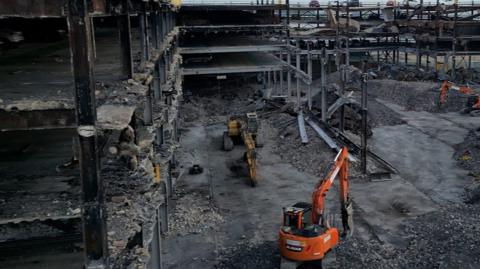 A digger stands in the charred wreckage of a multi-storey car park at Luton Airport.