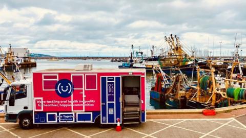 Red and white lorry with smiling logo at a harbour