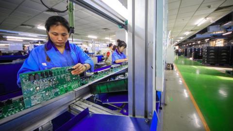 Worker with a circuit board in a Yamaha musical instrument factory in Tianjin