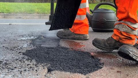 A person in hi-vis fixing a pothole in the road