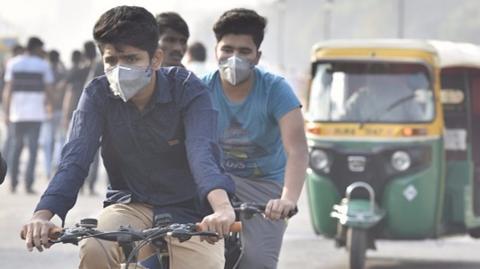 Men wearing masks ride bicycles in Delhi