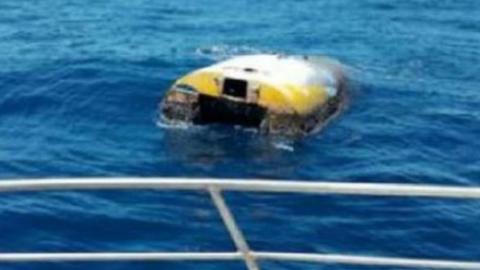 The upturned vessel Wild Eyes, seen from behind the rail of another boat