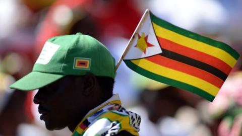 A Zimbabwean holds a national flag as he greets President Robert Mugabe