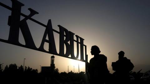 Silhouettes of people outside a sign for Kabul