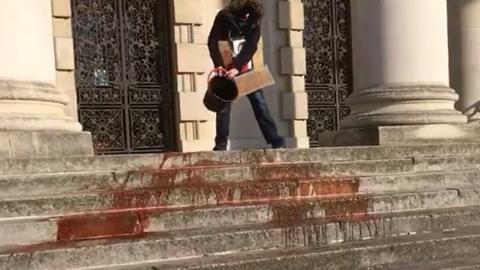 A woman pours a bucket of red liquid on the steps of Leeds Civic Hall