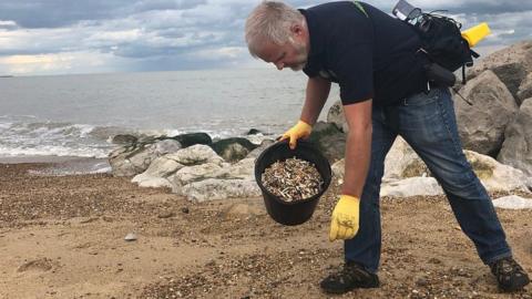 man picking up cigarette butts from a beach