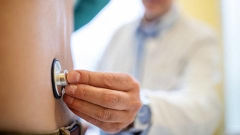 A doctor holding a stethoscope to someone's back