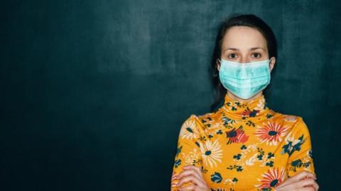 Woman in front of blackboard wearing a face cocering