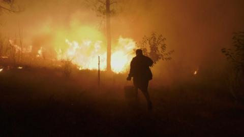 One person tries to put out the fire as it gets close to their house